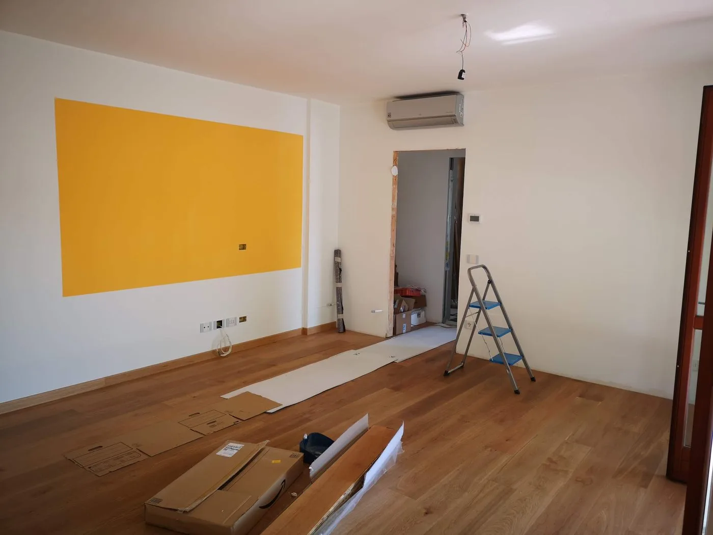 Interior de apartamento em reforma, com escada, ferramentas e piso de madeira.